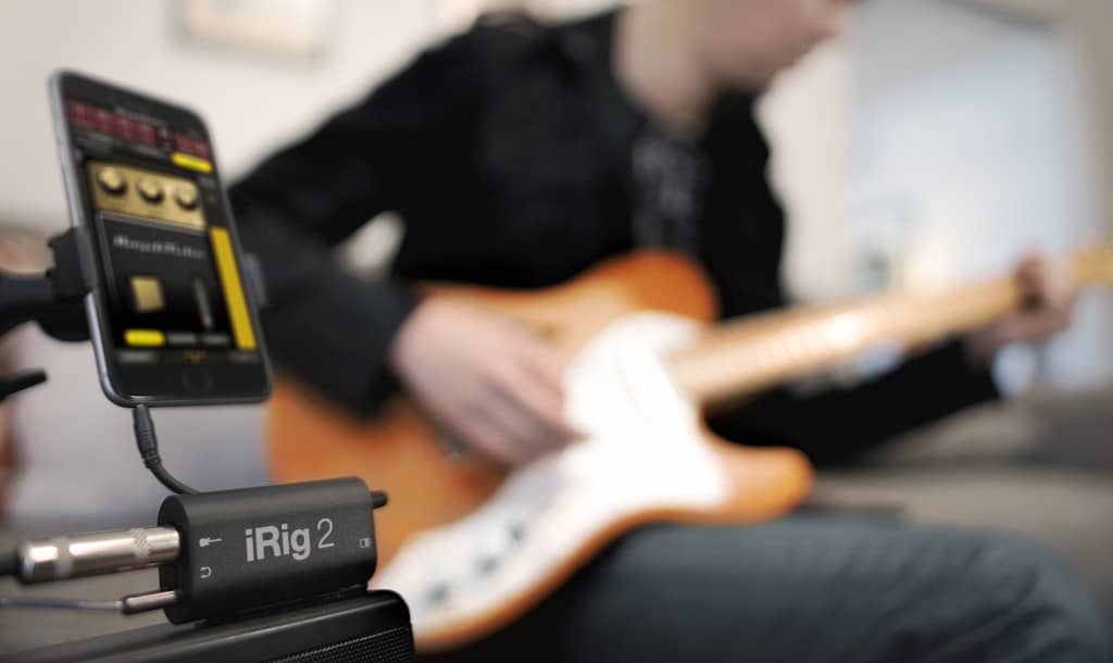 Hombre tocando una guitarra conectado al IK Multimedia iRig 2 con un móvil y a un amplificador